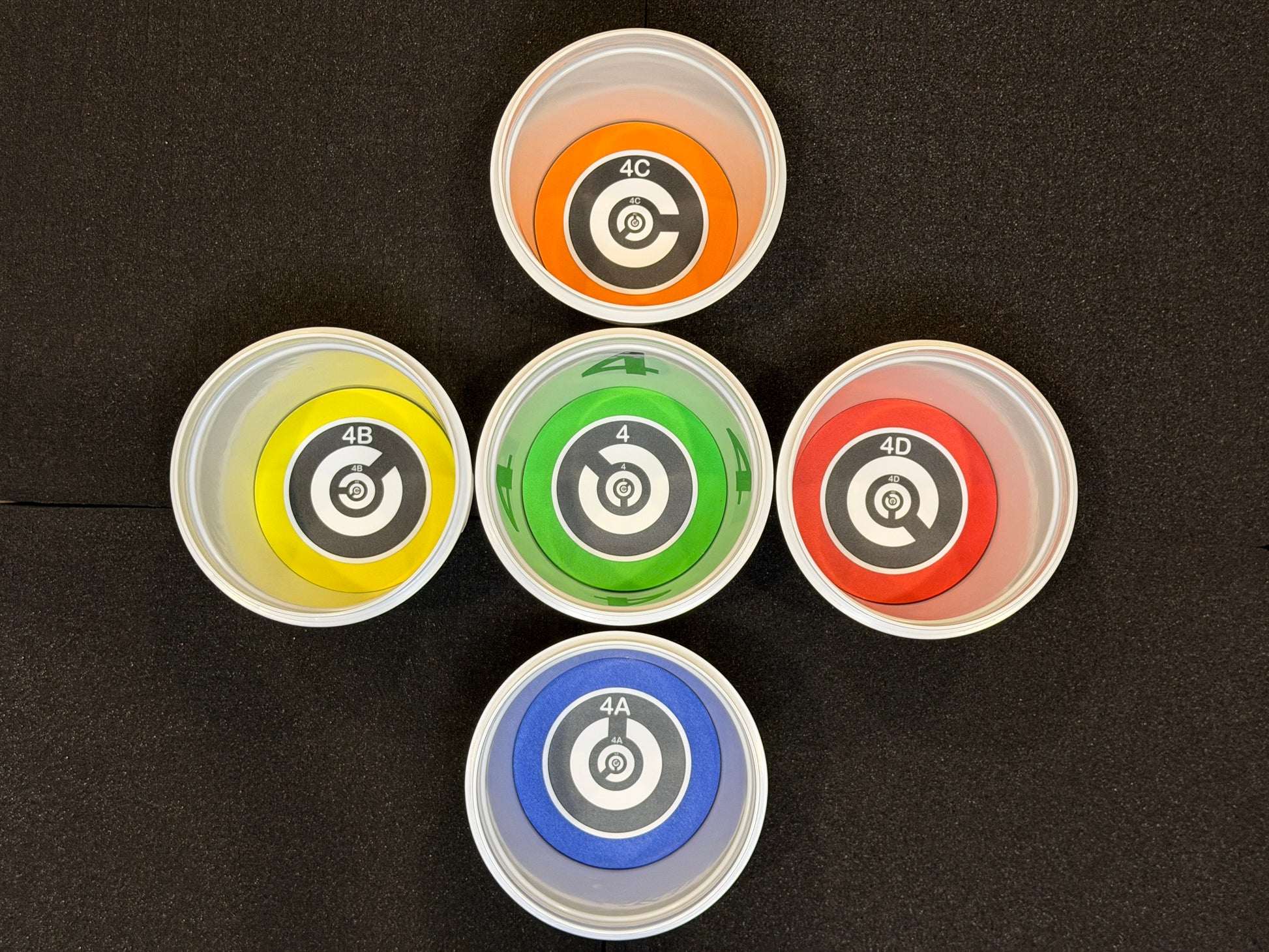 Six small plastic containers with colored lids on a black background